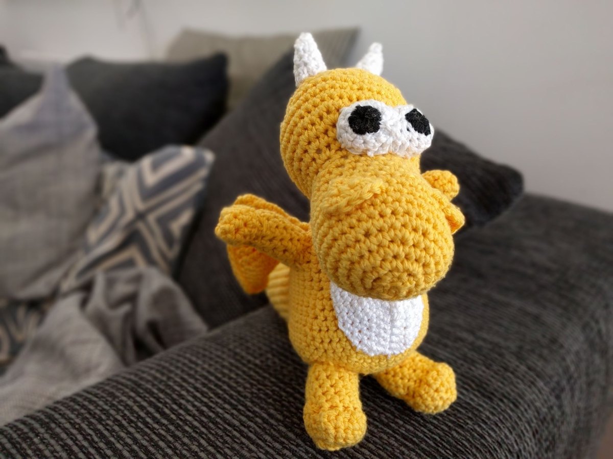 Gelber gehäkelter Amigurumi-Drache mit weißen Hörnern und weißem Bauch auf einem Sofa