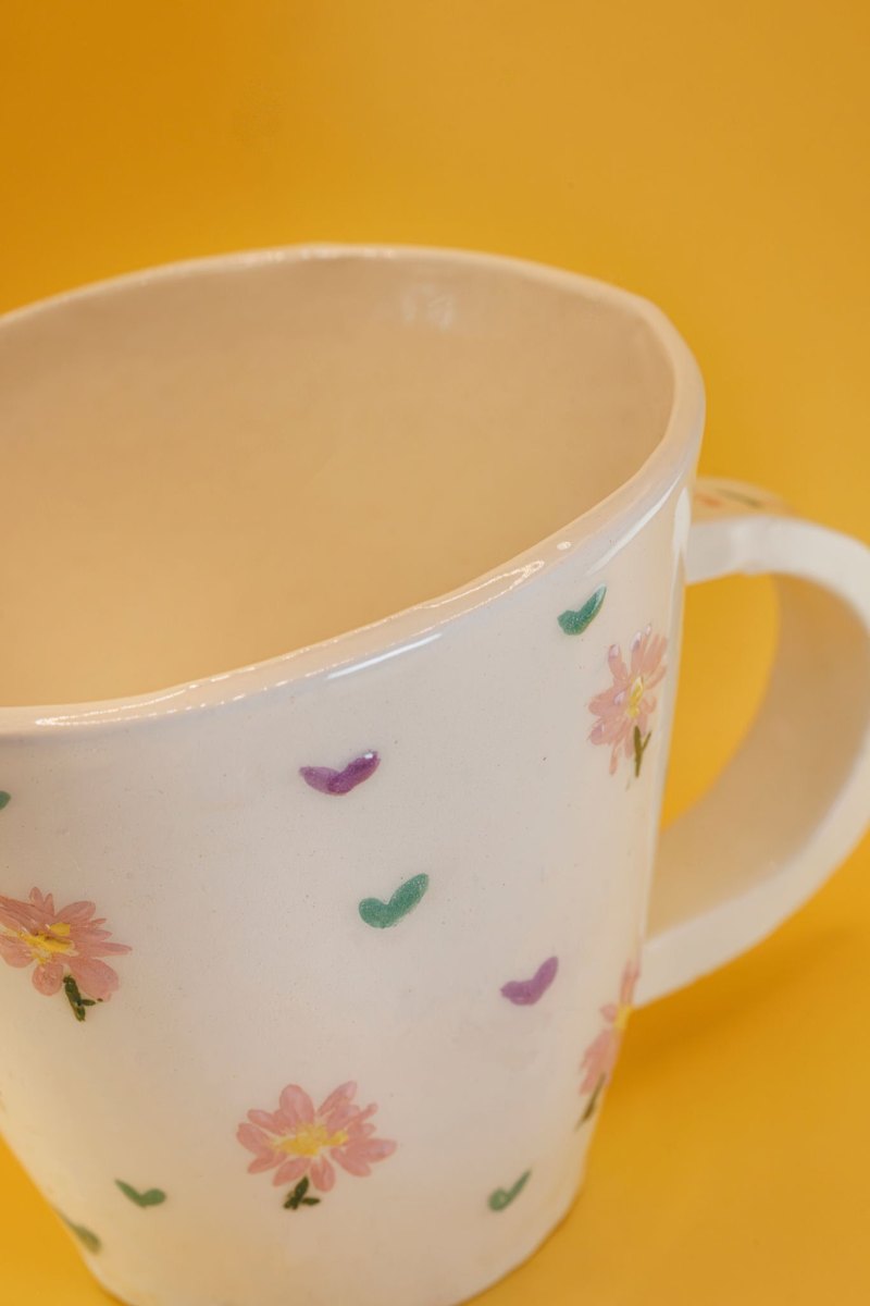Handbemalte weiße Keramiktasse mit zarten rosa Gänseblümchen und kleinen grünen Blättern