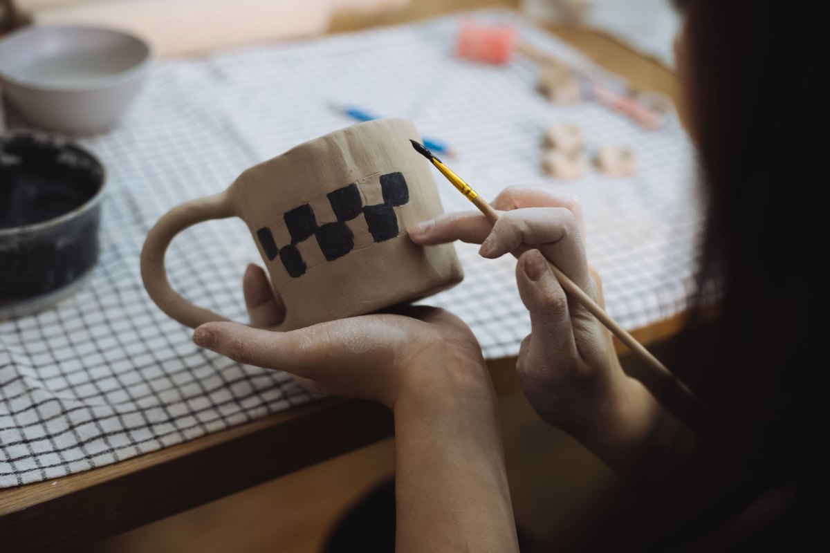 Künstlerin bemalt eine Keramiktasse mit einem präzisen geometrischen Muster am Tisch