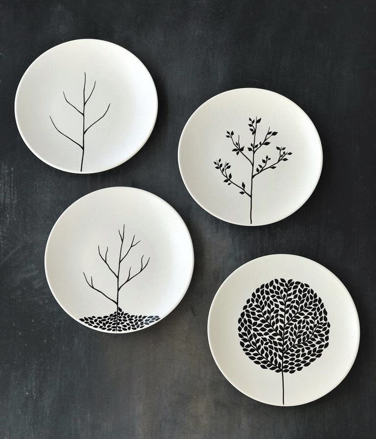 Vier weiße Keramikteller mit minimalistischen schwarzen Baummotiven
