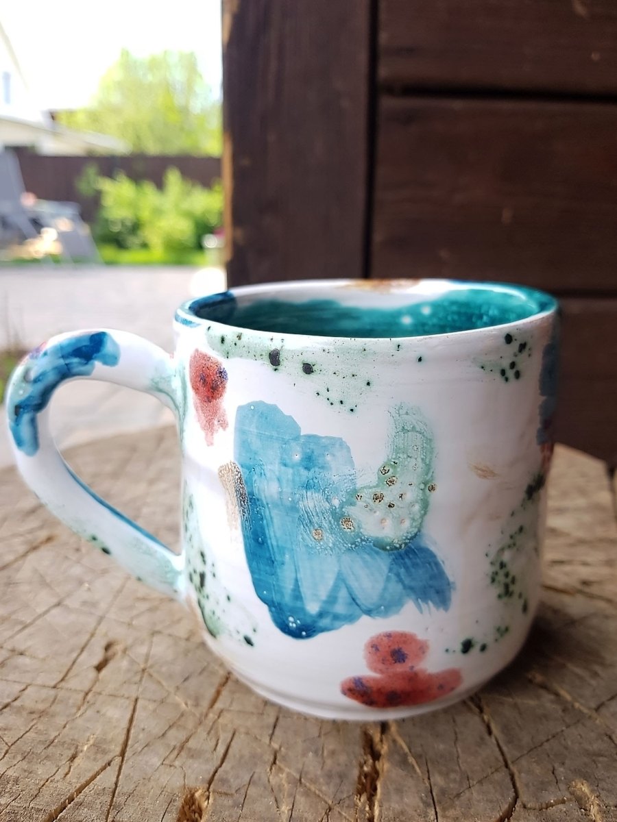 Handbemalte Keramiktasse mit türkisen und korallfarbenen Aquarell-Flecken und feinen Farbspritzern