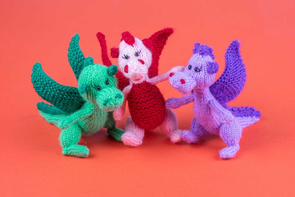 Drei kleine bunte Häkeldrachen in Grün, Rot-Weiß und Lila nebeneinander