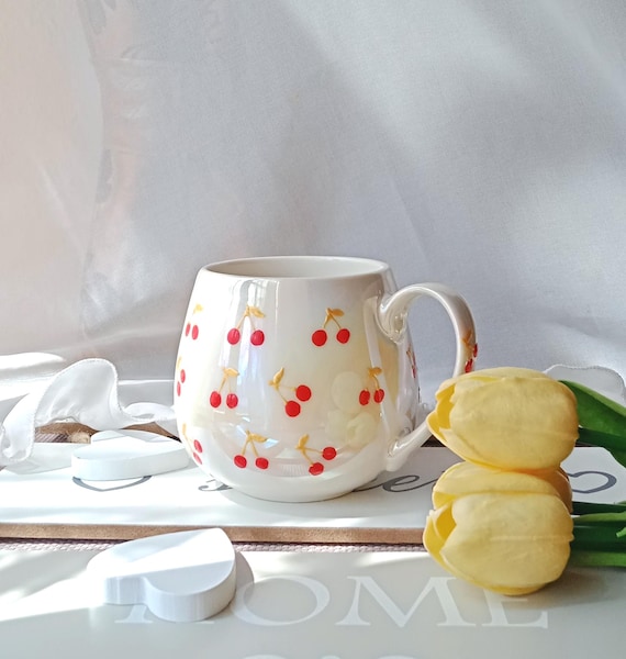 Weiße Keramiktasse bemalt mit vielen kleinen roten Kirschen und grünen Stielen