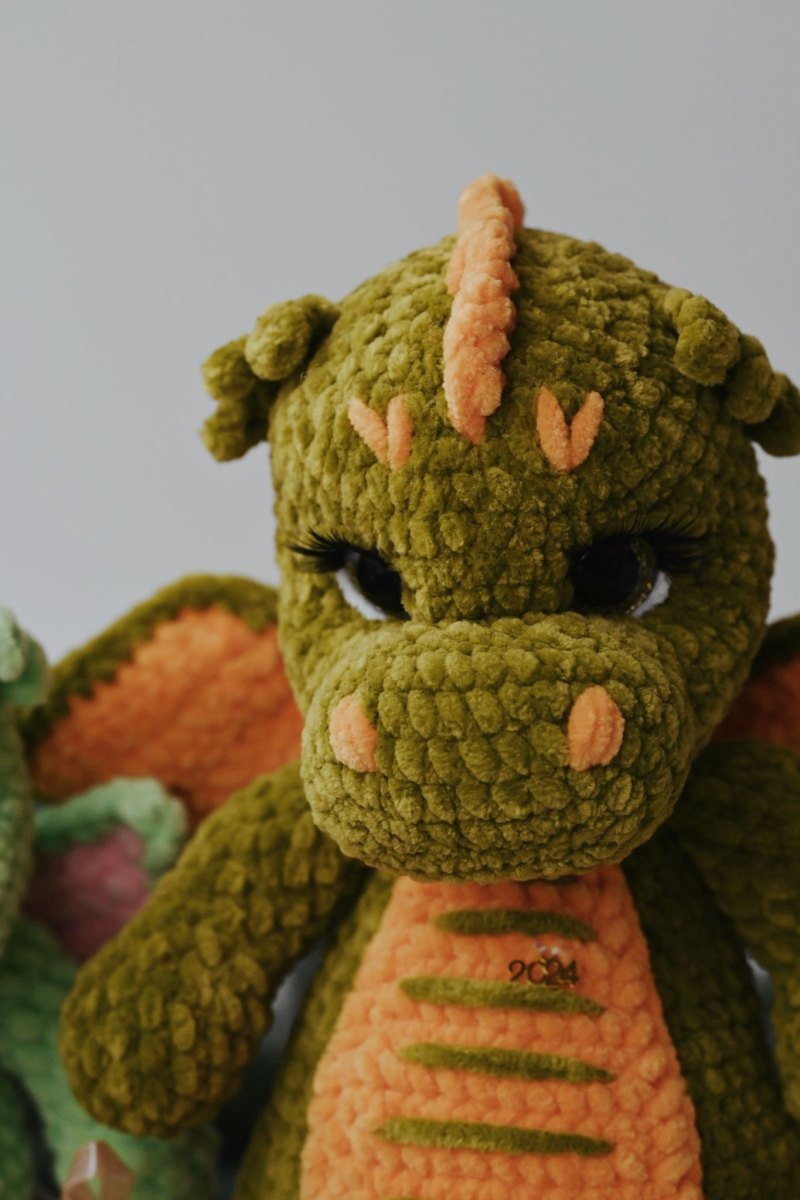 Nahaufnahme eines flauschigen Häkeldrachen aus olivgrünem und orangem Samtgarn