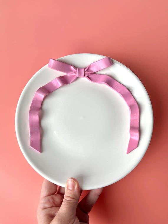 Kleiner weißer Keramikteller bemalt mit einer großen rosa Schleife am Rand