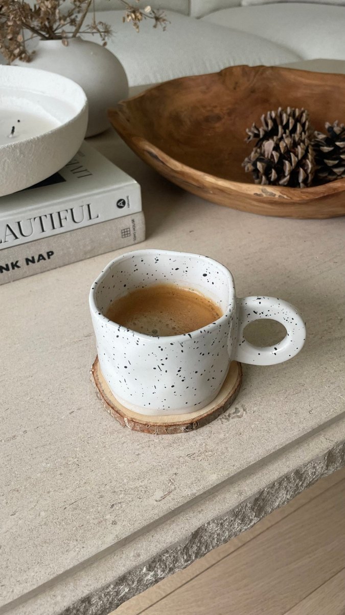 Weiße Espressotasse mit feinen schwarzen Farbsprenkeln auf einem Holzuntersetzer