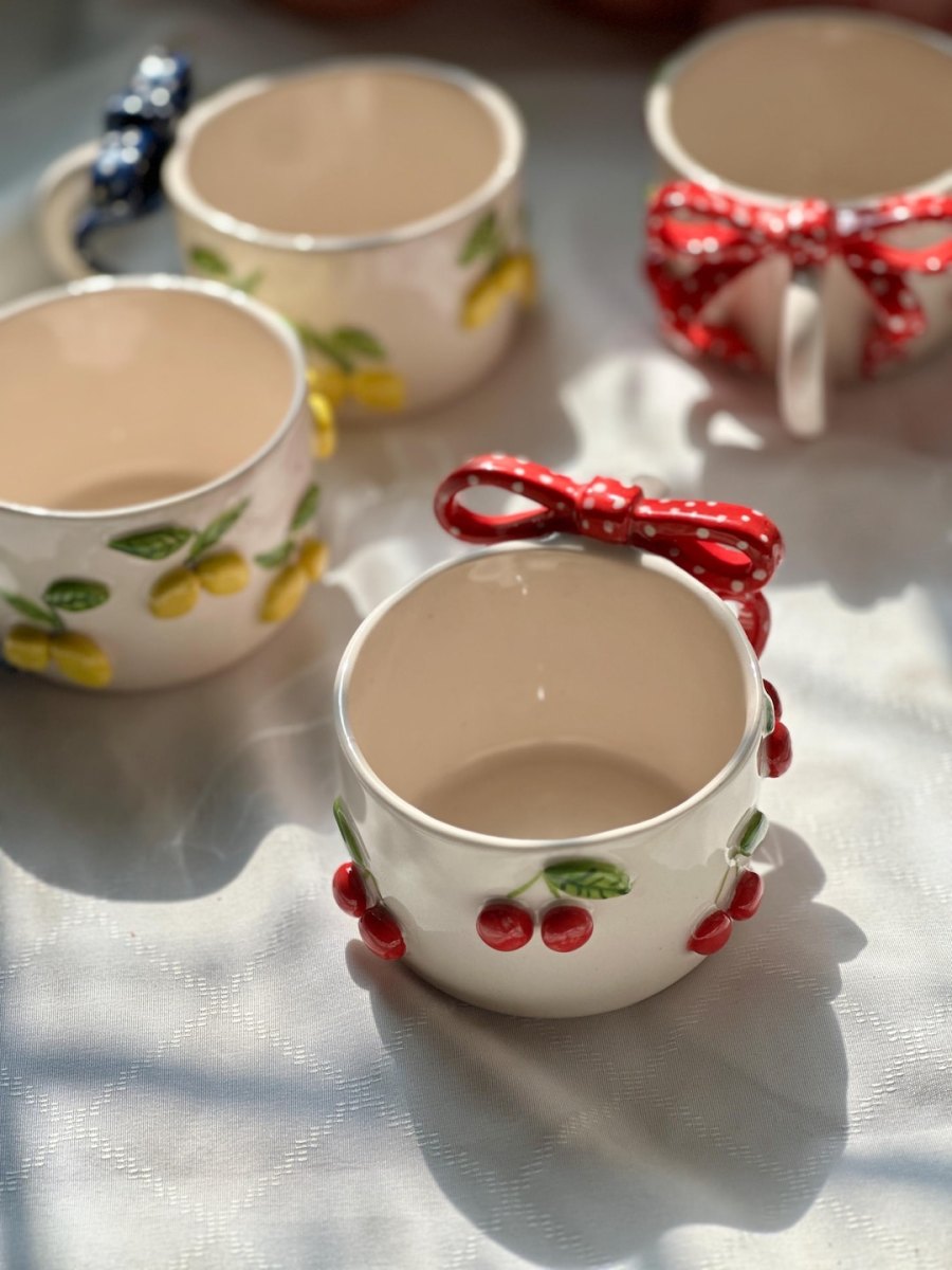 Weiße Keramiktasse mit aufgemalten roten Kirschen und rot-weiß gepunkteter Schleife am Henkel