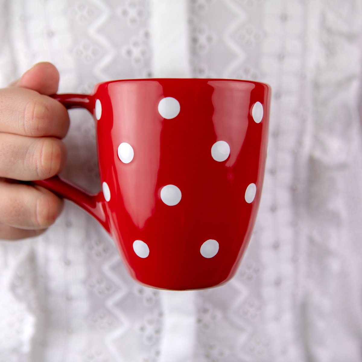 Kräftig rote Kaffeetasse mit gleichmäßigen weißen Punkten in der Hand