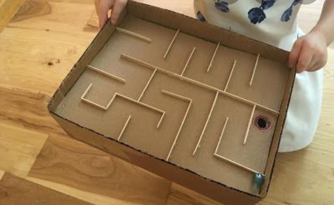 Flacher Karton mit einem Labyrinth aus Holzstäbchen, am Ende des Wegs ein Loch und eine kleine Murmel