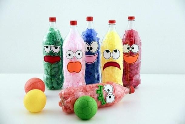 Fünf Plastikflaschen mit bunten Papierschnipseln gefüllt und mit Gesichtern beklebt in Grün, Rosa, Blau, Gelb und Rot, davor bunte Bälle und eine umgefallene Flasche