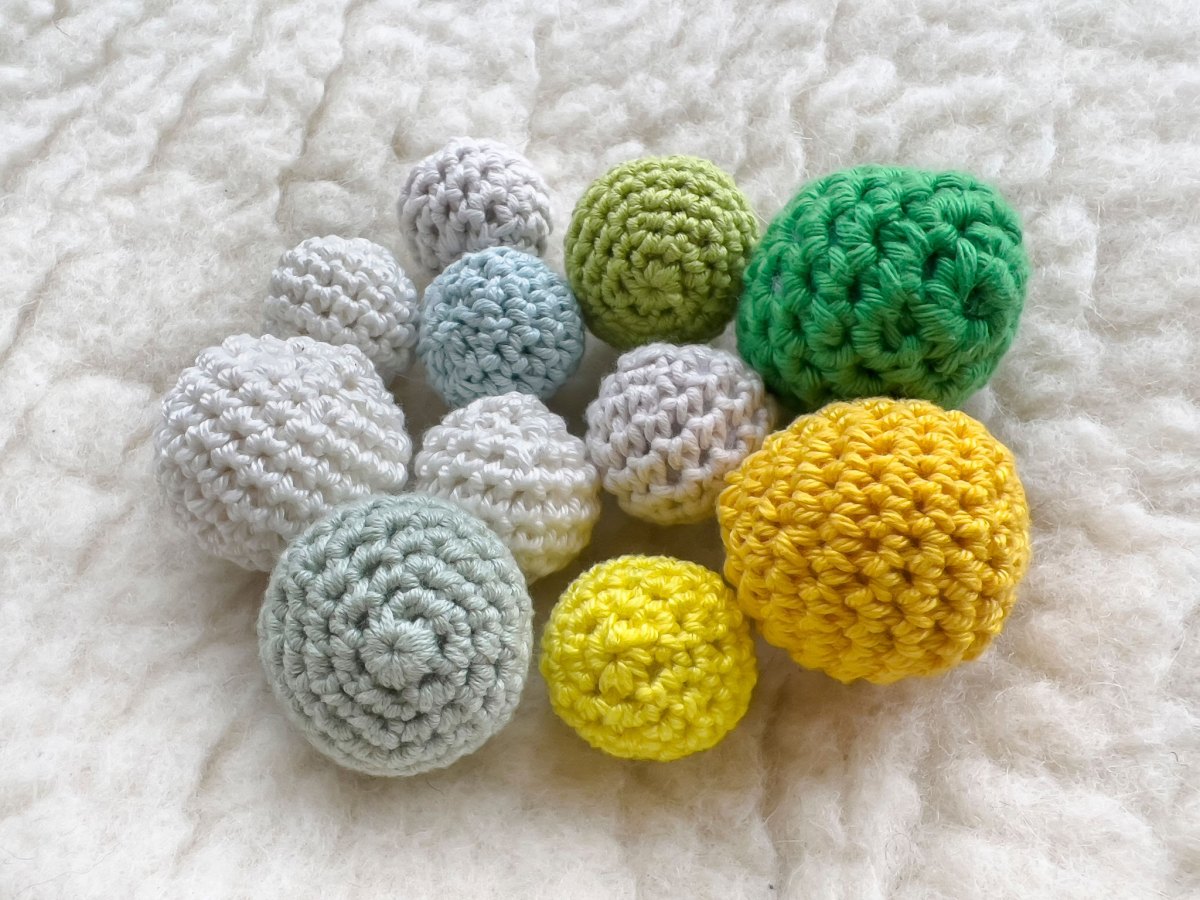 Verschieden große gehäkelte Amigurumi-Kugeln in Grün, Gelb und Blau